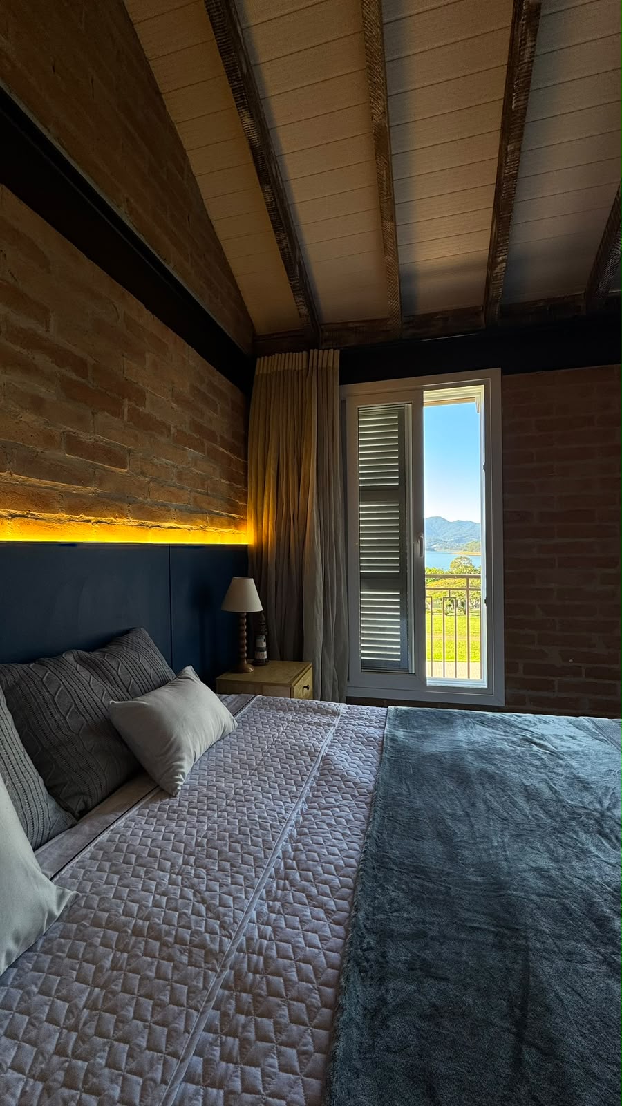 Quarto com painel de madeira e iluminação sobre a cabeceira