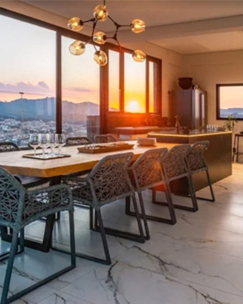 Sala de jantar com mesa de madeira e vista para as montanhas ao pôr do sol